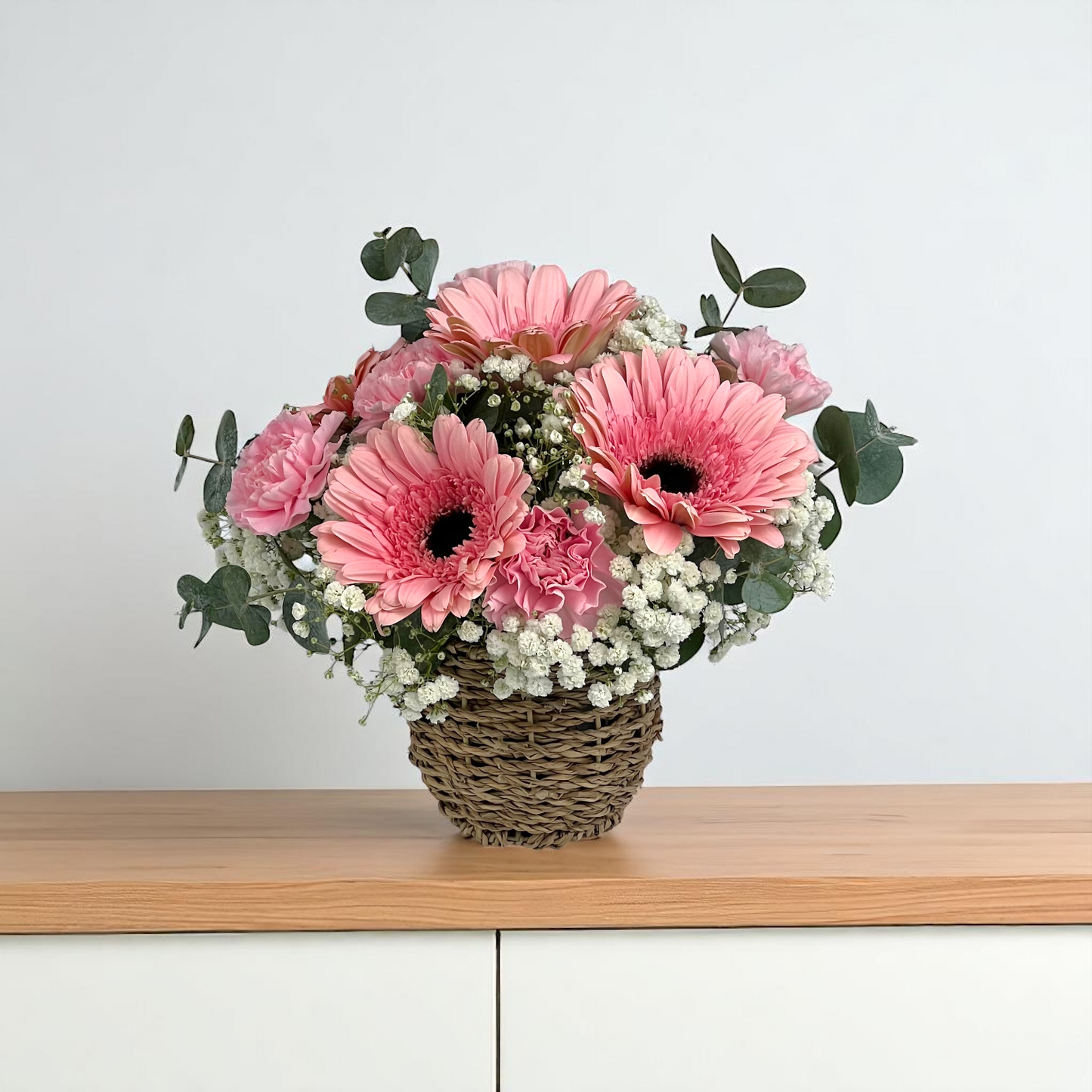 Front view of Sugar Petals flower basket featuring pink gerbera and pink carnations, arranged in a compact round basket.