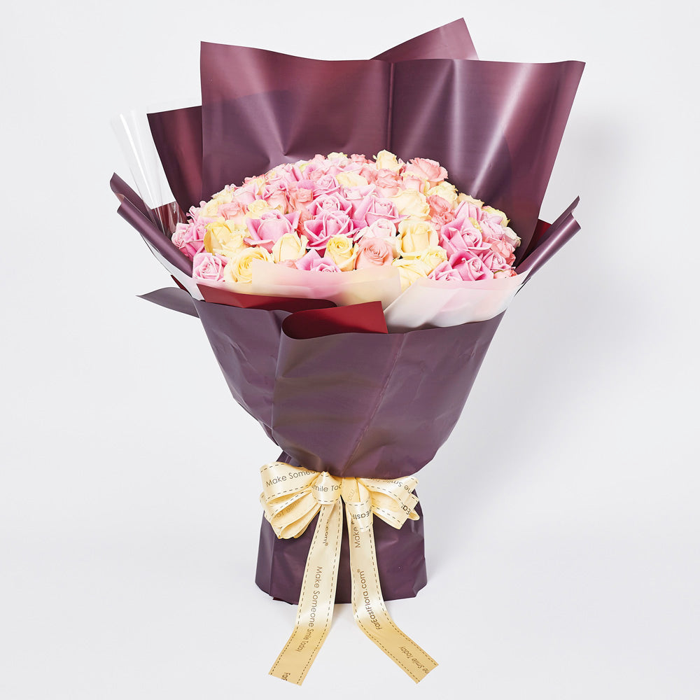 Everlasting Joy bouquet with 99 mixed pink, two-toned, and champagne roses wrapped in deep purple paper with a gold ribbon.