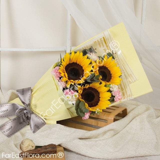 Sunflower Spa for Soul bouquet with three yellow sunflowers, pink carnations and eucalyptus foliage in pale yellow wrapping