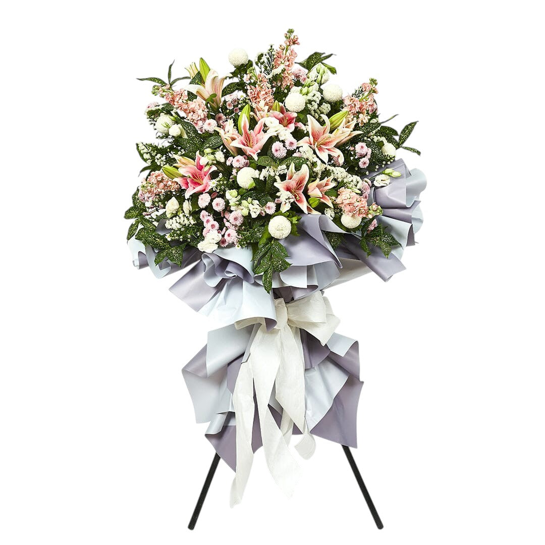 Floral arrangement with pink lilies and white flowers on a stand against a white background