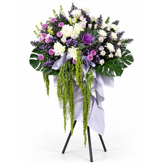Lavender Serenity condolence flower stand with light purple roses, white roselilies, purple brassica and purple chrysanthemums
