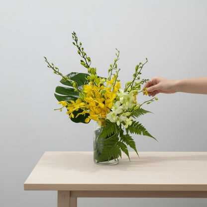 Yellow orchid flower arrangement in glass vase with green foliages on table 