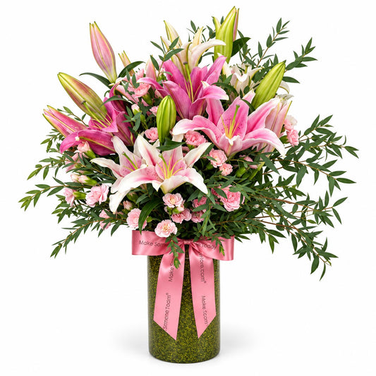 Lily Blush table flower arrangement with dark and light pink lilies, pink spray carnations and eucalyptus in a green vase with pink ribbon